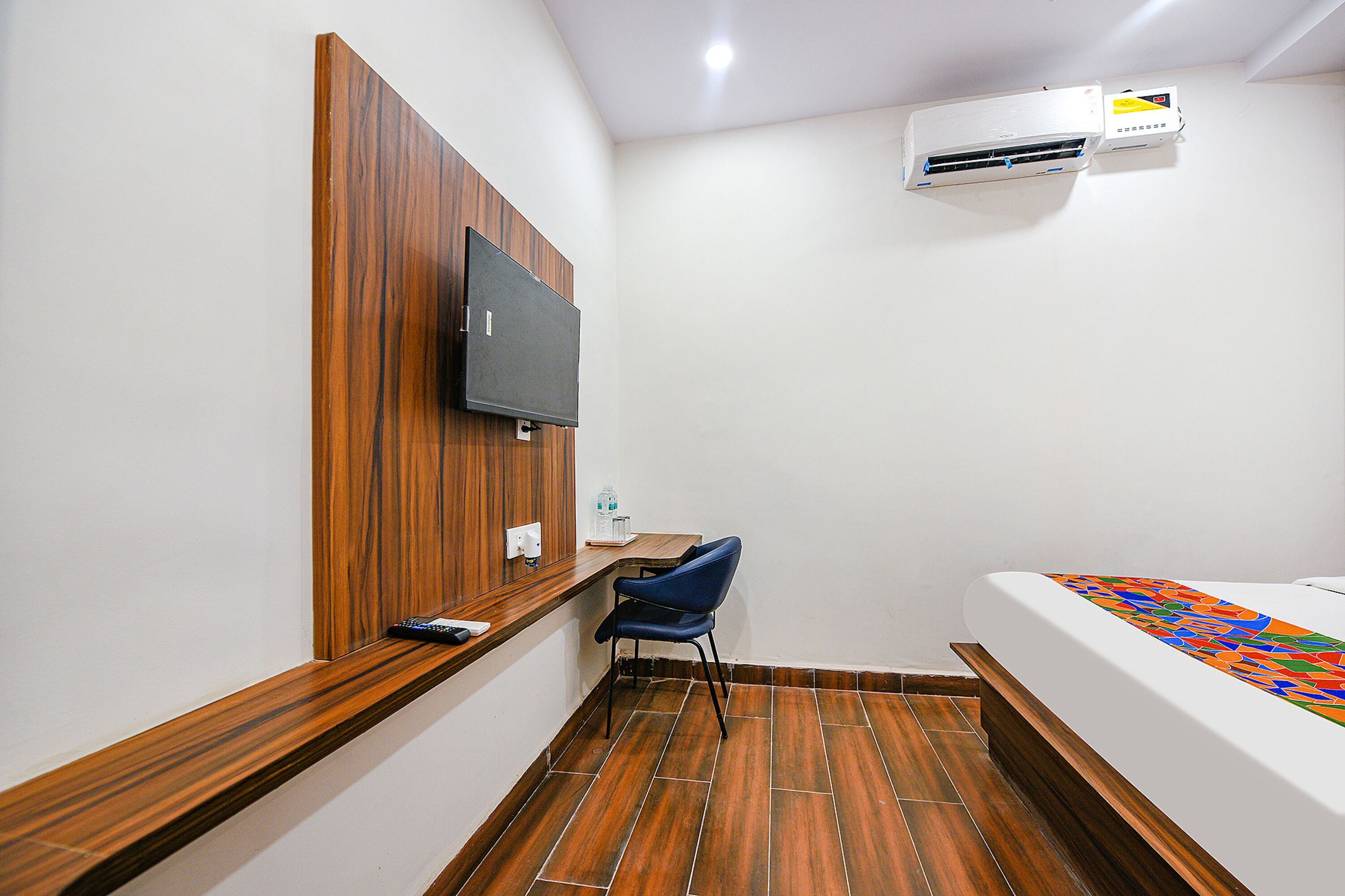 Een kleine kamer met een houten tv-meubel, een bureau, een stoel, een bed en een airconditioner.