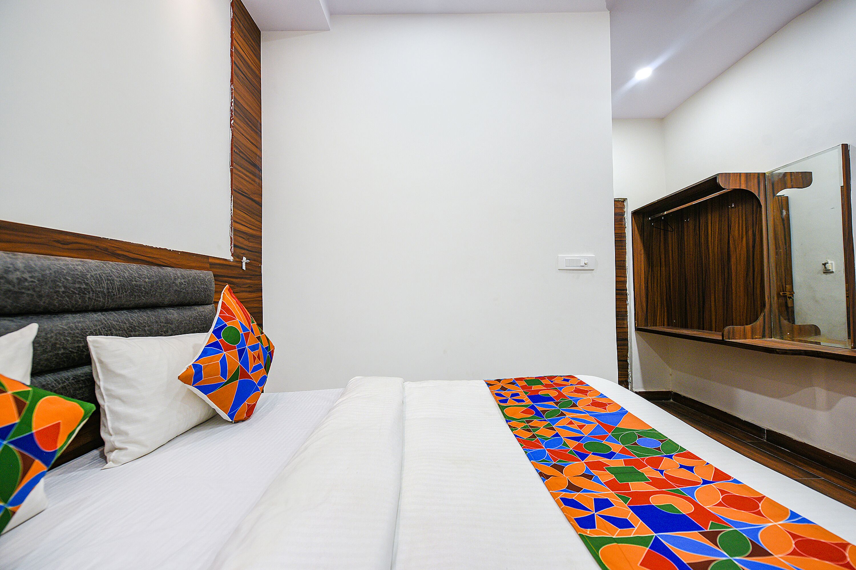 A hotel room with a bed, pillows, a wooden headboard, a mirror, and a patterned runner.