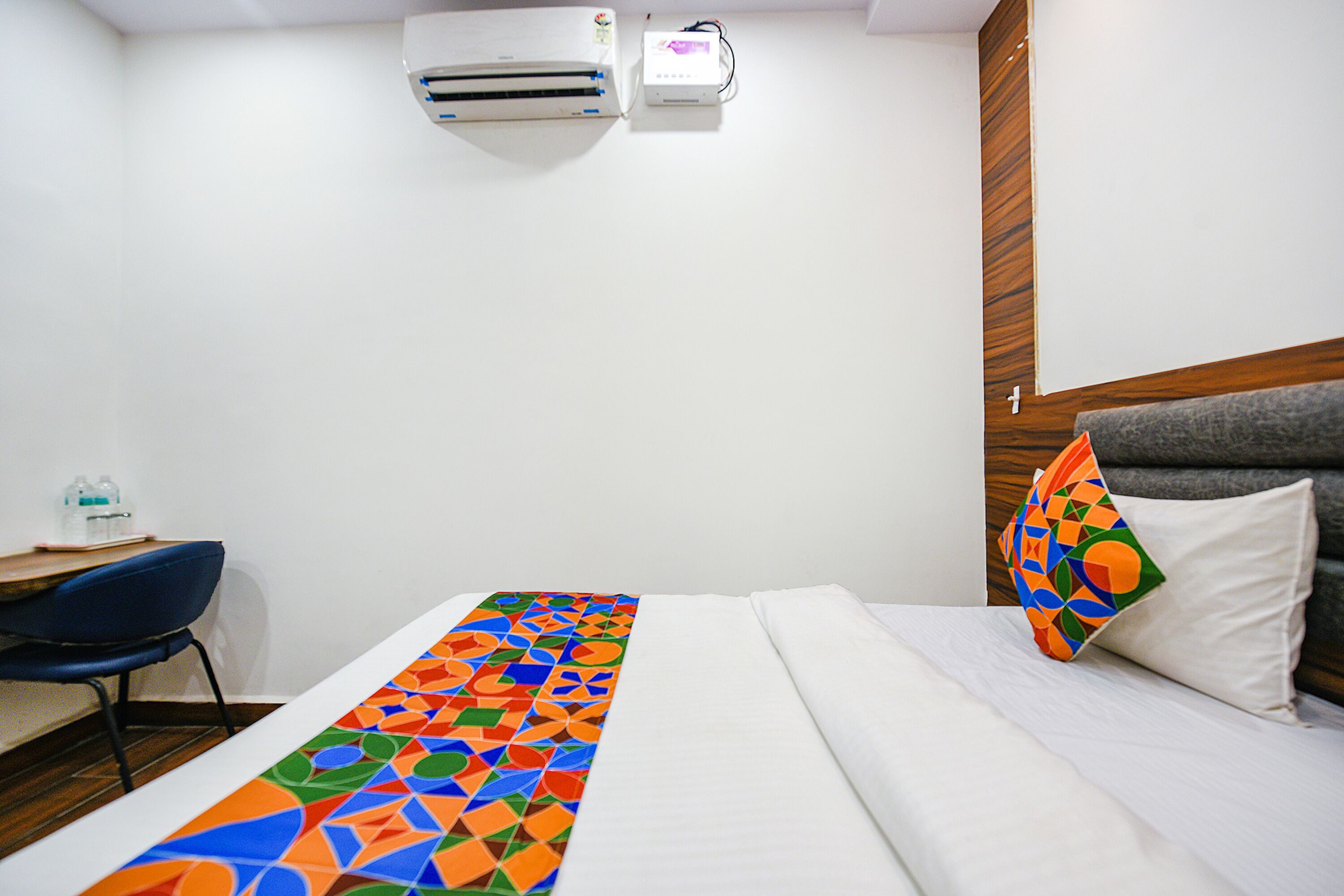 A hotel room with a bed, a desk, and an air conditioning unit.