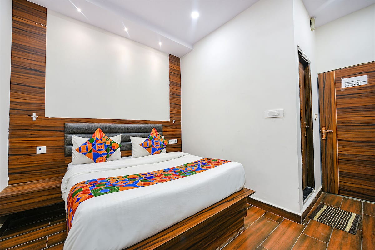 Una cama bien hecha con un edredón de estampado geométrico y colorido, un cabecero de madera y dos almohadas decorativas.