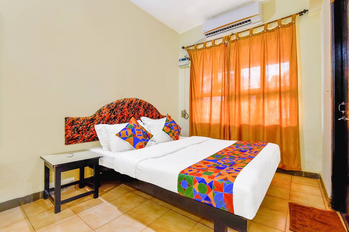 Quarto de hotel com cama, mesa de cabeceira, aparelho de ar condicionado e janela com cortinas.