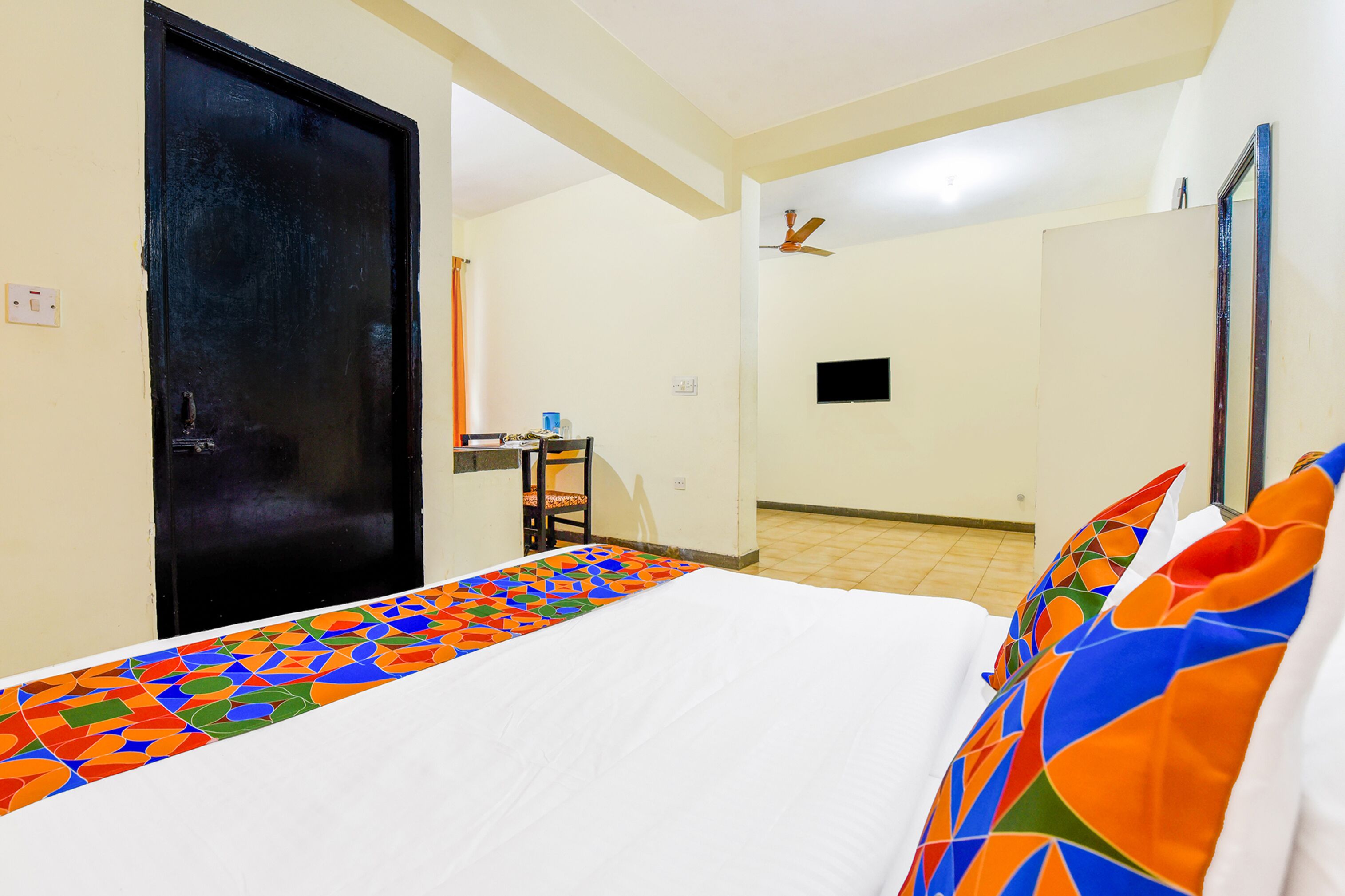 A hotel room with a bed, a chair, a desk, and a door.