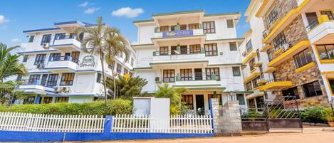 A multi-story hotel with balconies and a white picket fence in front.