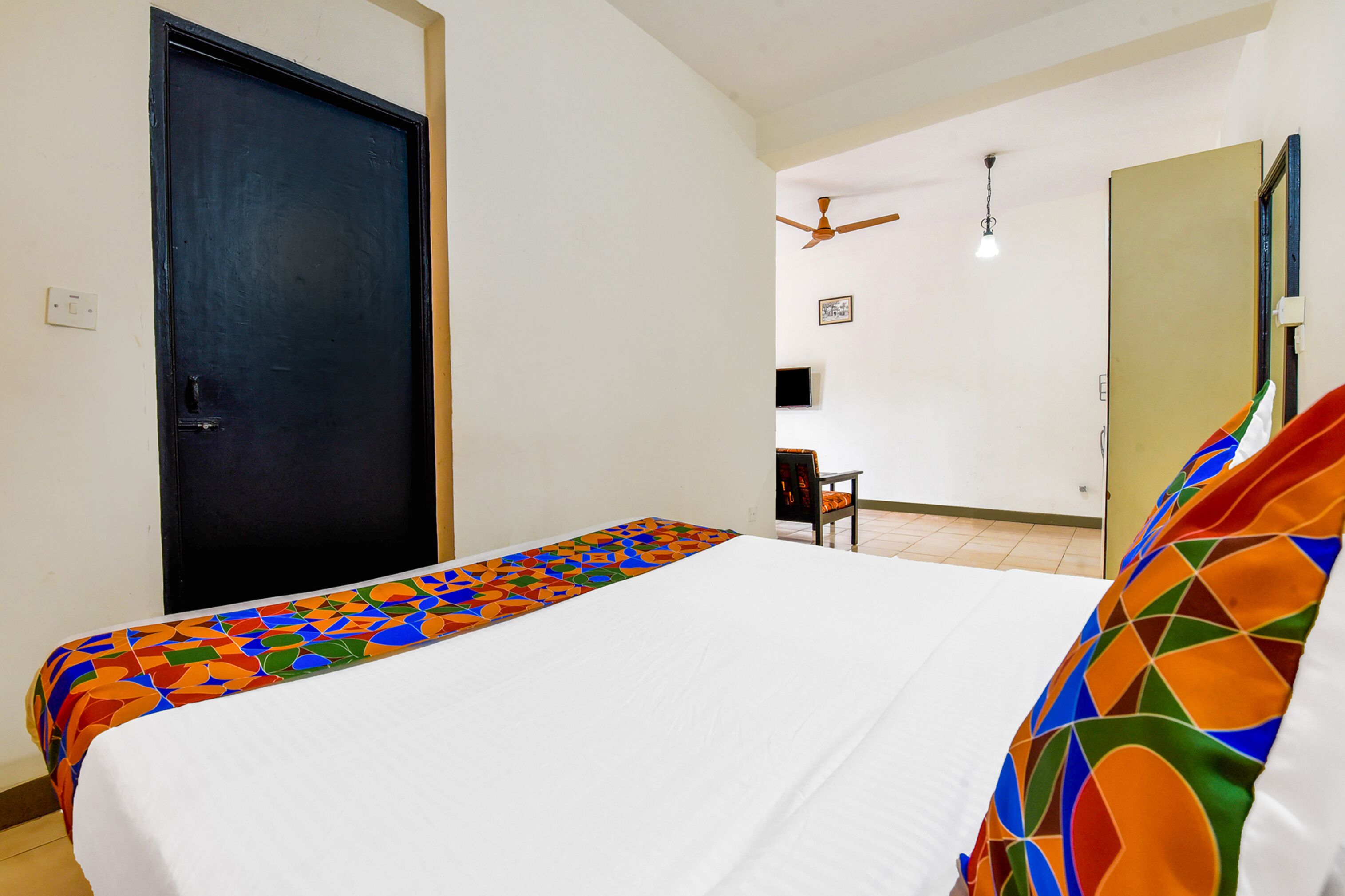 Ein Hotelzimmer mit Bett, Schreibtisch, Stuhl, Deckenventilator und einer Tür.