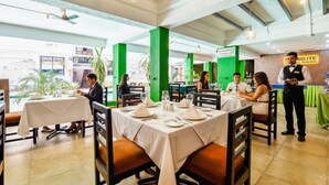Un restaurante con mesas dispuestas para comer, un camarero atendiendo a los comensales y un letrero que indica el nombre del restaurante.