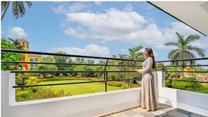 Un balcón con vista a un jardín cuidado y un edificio amarillo a lo lejos.