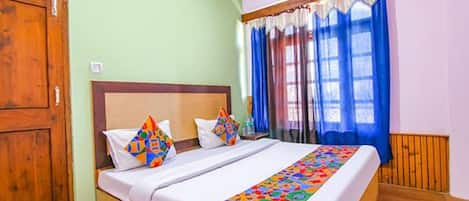 A neatly made bed with colorful pillows and a patterned bed runner, a wooden wardrobe, and a window with blue curtains.