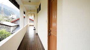 A corridor with a wooden door, a tiled floor, and a window overlooking a building with a red roof. - Fabhotel Mahavir (Manali)