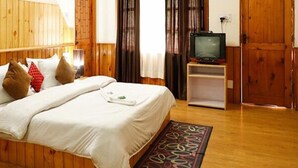 A wooden-paneled room with a bed, a television on a stand, and a small wooden cabinet. - Fabhotel Mahavir (Manali)