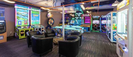 A gaming arcade with various machines, including a bowling game, and seating areas with cushioned chairs.