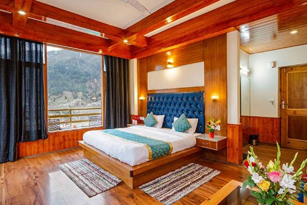 A wooden-floored bedroom with a large bed, a view of the outdoors, and a wooden headboard.