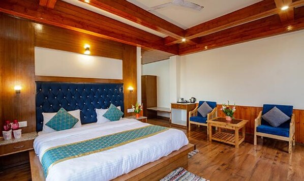A hotel room with a large bed, wooden ceiling, and a seating area with two chairs and a small table. - Fabhotel La Kailasha Regency (Manali)