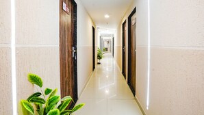 A hotel corridor with wooden doors, a shiny tiled floor, and potted plants. - Fabhotel Royal Paradise (Surat)