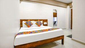 A modern hotel room with a wooden bed frame, white bedding, and a colorful geometric-patterned throw. - Fabhotel Royal Paradise (Surat)
