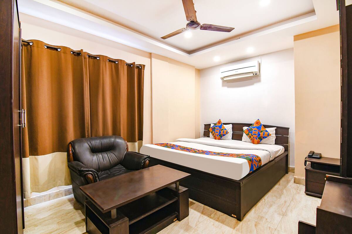 A hotel room with a bed, a leather armchair, a wooden coffee table, and a ceiling fan.