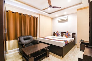 Una habitación de hotel con una cama, un sillón de cuero, una mesa de centro de madera y un ventilador de techo.