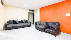 A living room with two sofas and a leather armchair, a white tiled floor, and an orange accent wall. - Fabhotel White Palace (Kolkata)