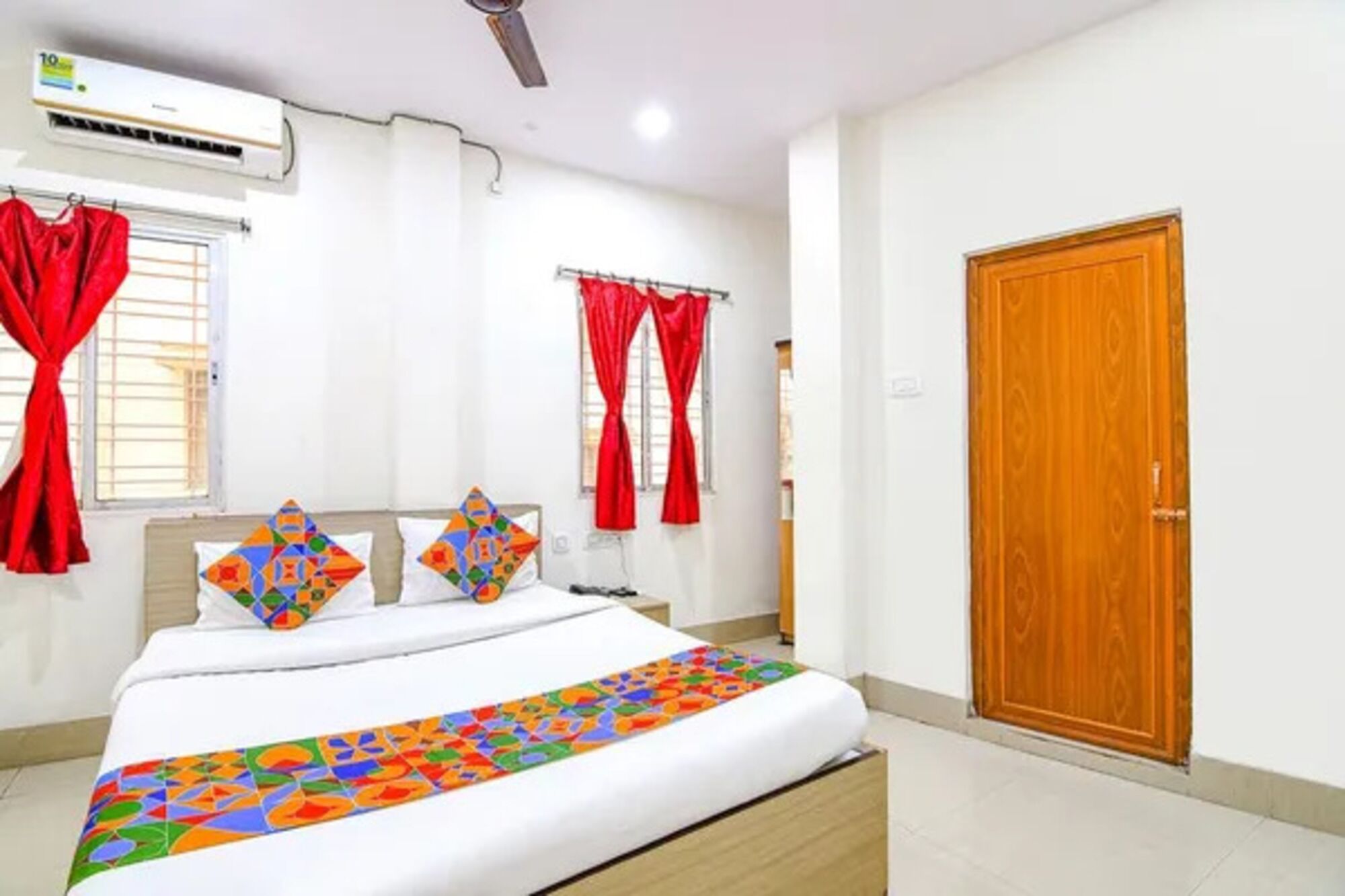 A bedroom with a bed, red curtains, a wooden door, and an air conditioning unit.