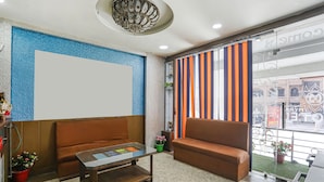 A hotel lobby with two brown sofas, a glass coffee table, a chandelier, and a large window with striped curtains. - Fabexpress Myraa (Mathura)