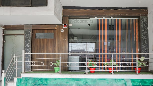 A hotel entrance with a wooden door, a balcony with metal railings, and potted plants. - Fabexpress Myraa (Mathura)