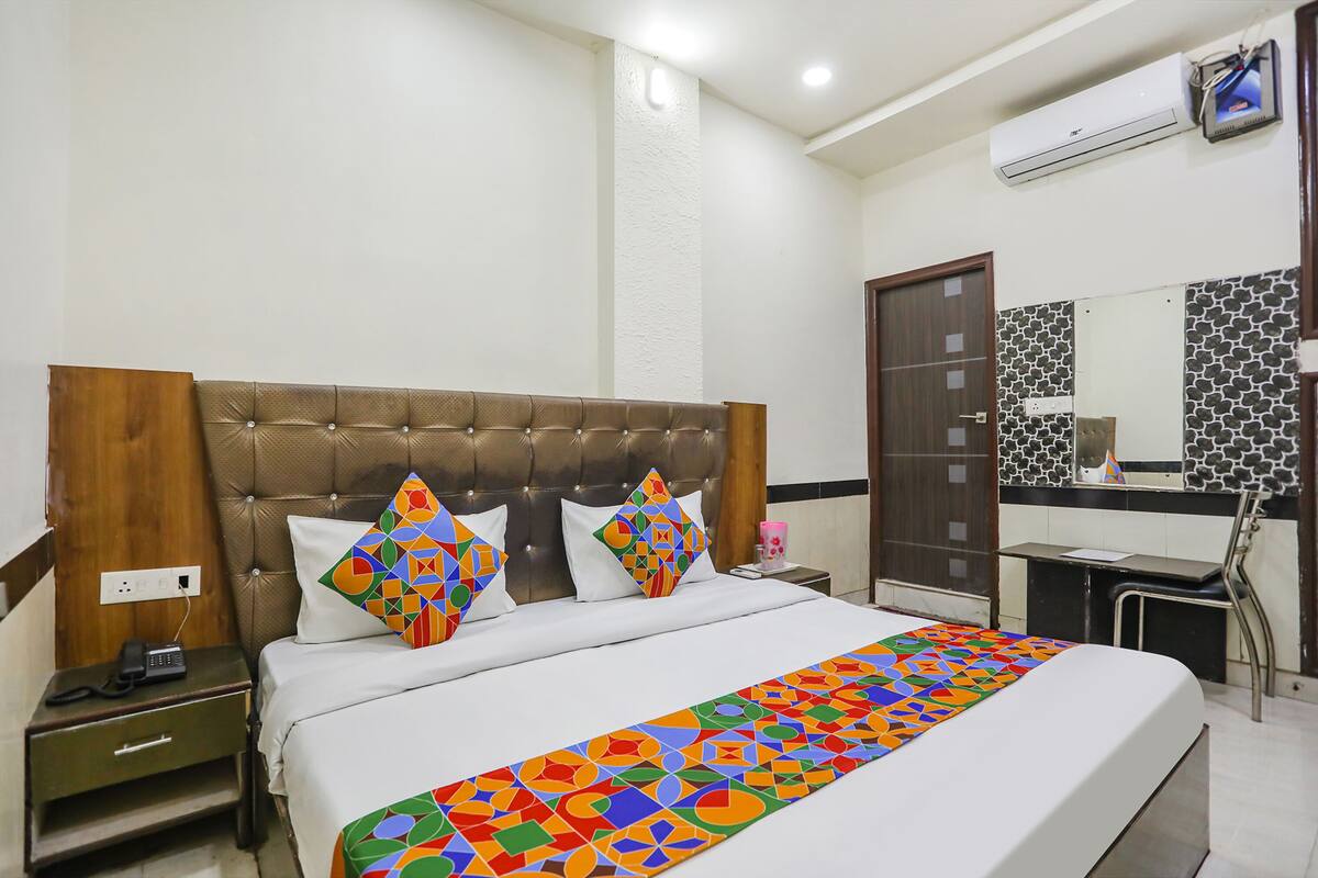 A hotel room with a tufted headboard, a bed with colorful geometric bedding, a bedside table with a phone, and a mirror with a patterned backsplash.