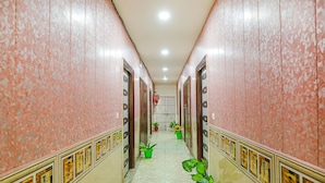 A corridor with pink patterned walls, green potted plants, and framed pictures on the walls. - Fabexpress Myraa (Mathura)
