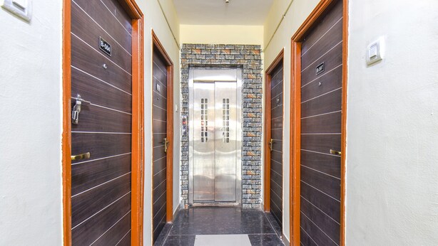 A hallway with two doors, each marked with a room number, leading to an elevator. - FabHotel Shri Krishna (Paud)