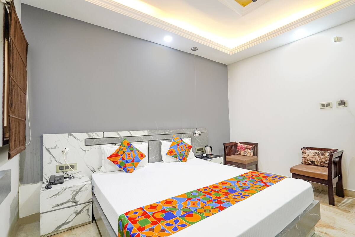 Una habitación de hotel con una cama grande, una mesita de noche de mármol, una silla y una pequeña mesa con lámpara.