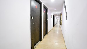 A long, narrow hallway with doors marked with numbers, white walls, and a tiled floor. - Fabhotel Santro (Ahmedabad)