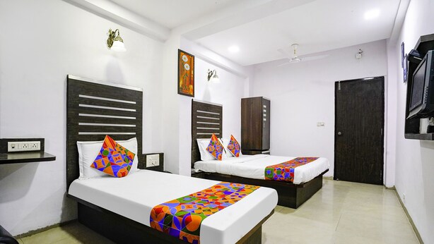 A hotel room with two beds, a wardrobe, a TV, and a painting on the wall. - Fabhotel Santro (Ahmedabad)