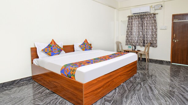 A hotel room with a wooden bed, a desk with a chair, and a patterned curtain. - Fabexpress Ashoka Lodging (Chhatrapati Sambhajinagar)