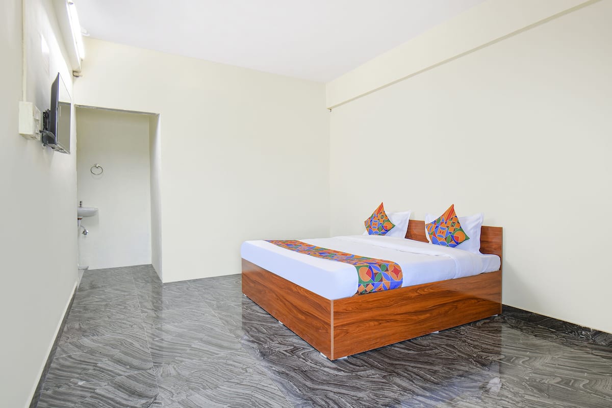 A bedroom with a wooden bed, white walls, a grey floor, and a TV mounted on the wall.