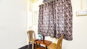 A small room with a table and two chairs, an air conditioning unit, a patterned curtain, and a wall socket. - Fabexpress Ashoka Lodging (Chhatrapati Sambhajinagar)