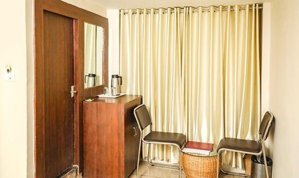 Una habitación con un escritorio de madera, dos sillas, un espejo y una ventana con persianas verticales.