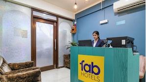 A reception desk with a sign reading "fab hotels" in a hotel lobby with patterned sofas and a blue wall. - Fabhotel Grand Hazra Inn (Kolkata)