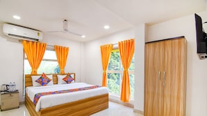 A hotel room with a wooden bed, orange curtains, a wardrobe, and an air conditioning unit. - Fabhotel Grand Hazra Inn (Kolkata)