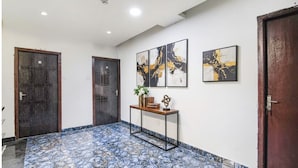 A hallway with patterned flooring, two wooden doors, a console table with decorative items, and three abstract paintings on the wall. - Fabhotel Grand Hazra Inn (Kolkata)