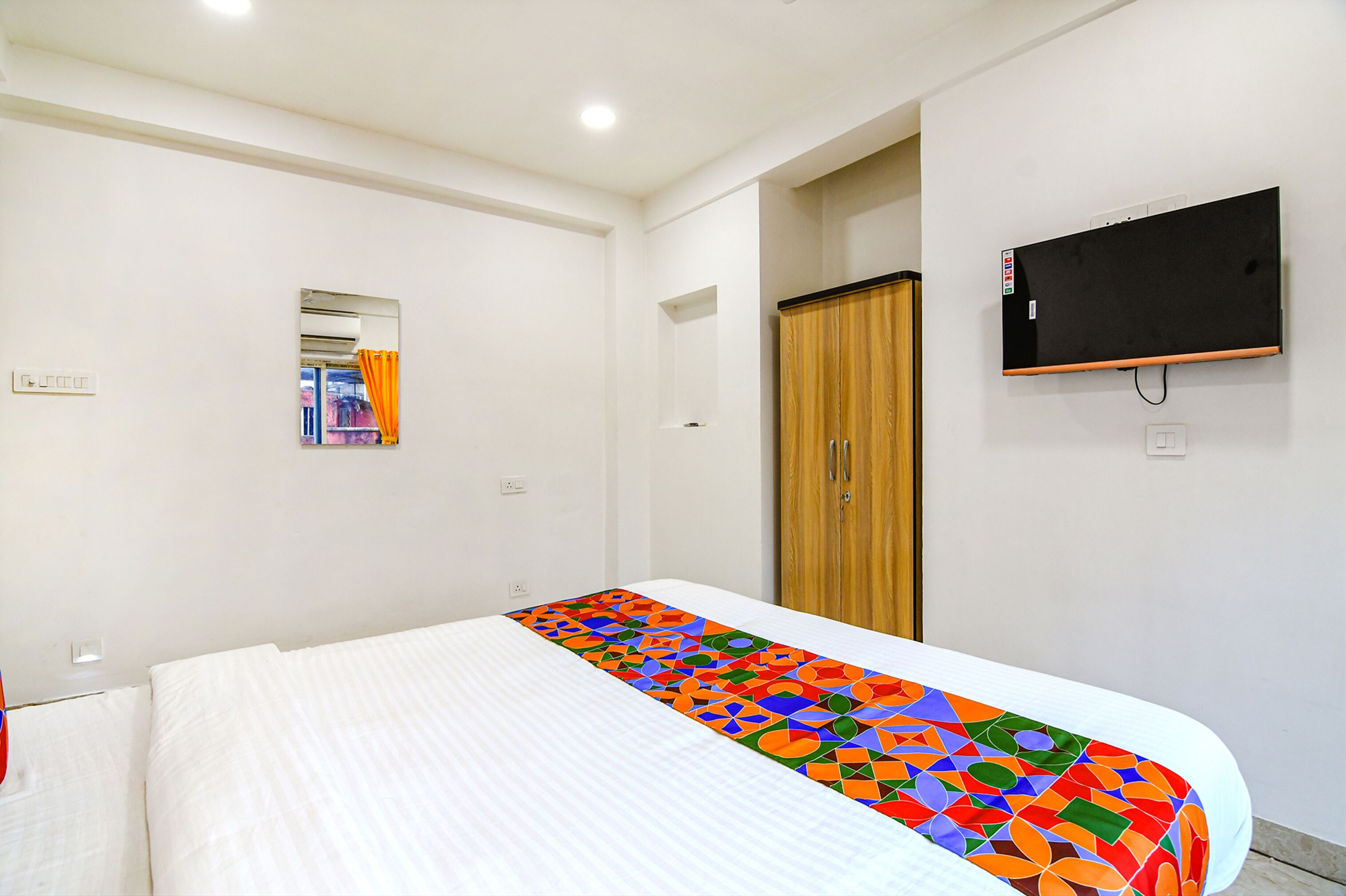 Una habitación de hotel con una cama, un televisor fijado a la pared y un armario de madera.