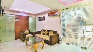 A modern room with a glass partition, a sofa, a glass coffee table, and a ceiling light fixture. - Fabhotel Royal Ville (Patna)