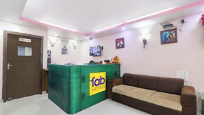 A reception area with a green counter, a brown sofa, clocks, and a TV on the wall. - Fabhotel Royal Ville (Patna)