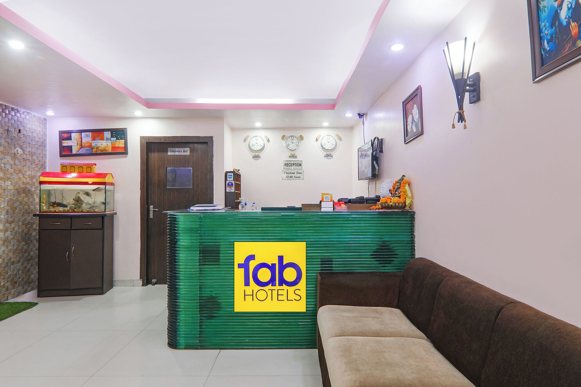 A reception desk with a 'fab hotels' sign, a reception area with a brown sofa, a clock, and a reception desk with a computer monitor.