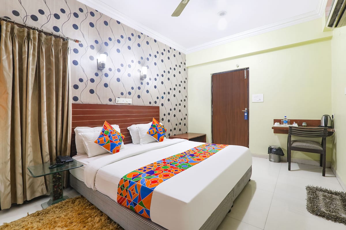 Quarto de hotel com uma cama, uma escrivaninha, uma cadeira, um telefone e um cesto de lixo.