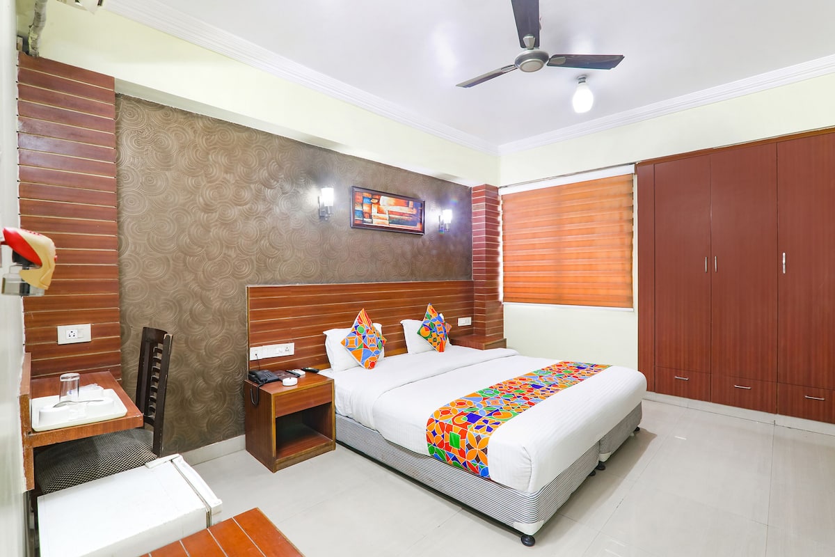Um quarto com cama, mesas de cabeceira, escrivaninha, guarda-roupa e ventilador de teto.