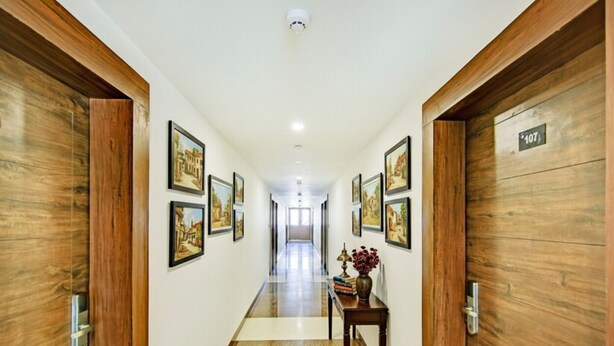 A hotel hallway with wooden doors, numbered room signs, and framed pictures on the walls. - Fabhotel Downtown Residency (Prayagraj)