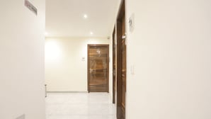 A hallway with a wooden door at the end, a 'No Smoking' sign, and a light switch on the wall. - Fabexpress Baba'S Inn (New Delhi)