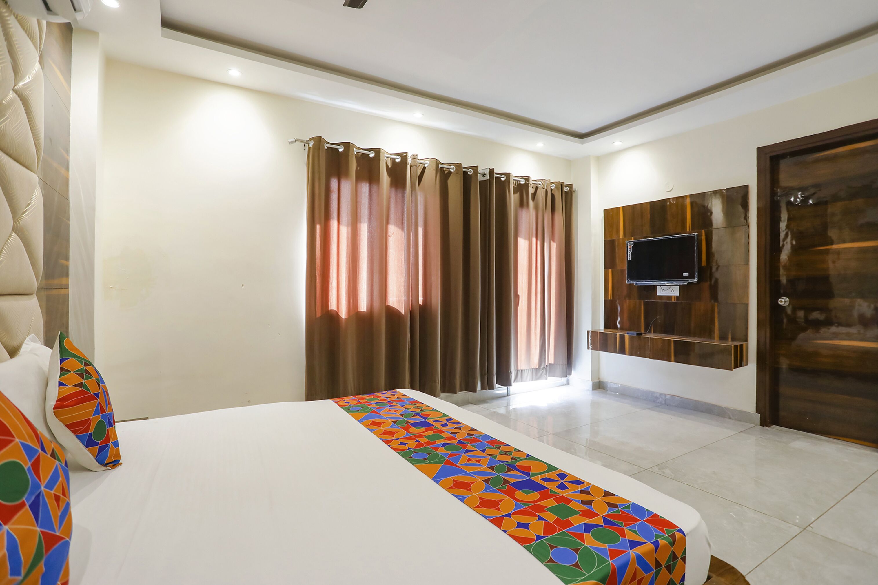 A hotel room with a large bed, a TV mounted on the wall, and a window with curtains.