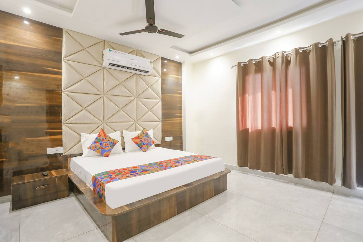 A modern hotel room with a large bed, a ceiling fan, an air conditioning unit, and a view of the outside through curtains.