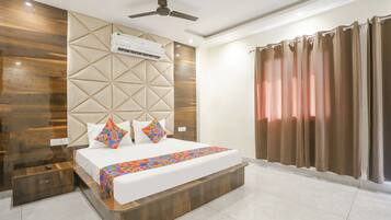 A modern hotel room with a large bed, a ceiling fan, an air conditioning unit, and a view of the outside through curtains.