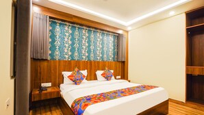 Une chambre d’hôtel moderne avec une tête de lit en bois, un grand lit recouvert d’une couverture colorée, une table de chevet avec un téléphone et une armoire.