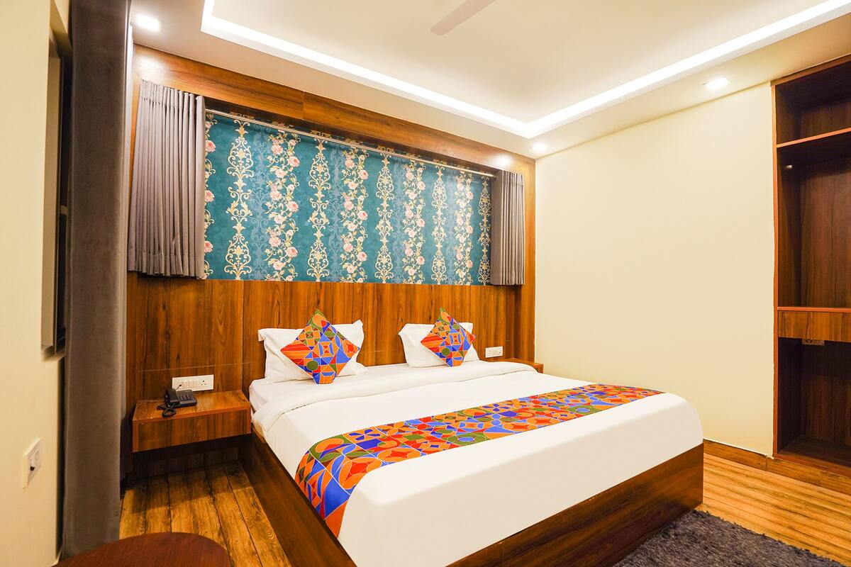 Ein modernes Hotelzimmer mit einem hölzernen Kopfteil, einem großen Bett mit bunter Decke, einem Nachttisch mit Telefon und einem Kleiderschrank.